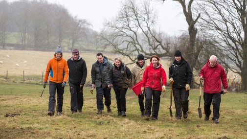 Group of people in winter work gear, walking across field while carrying tools